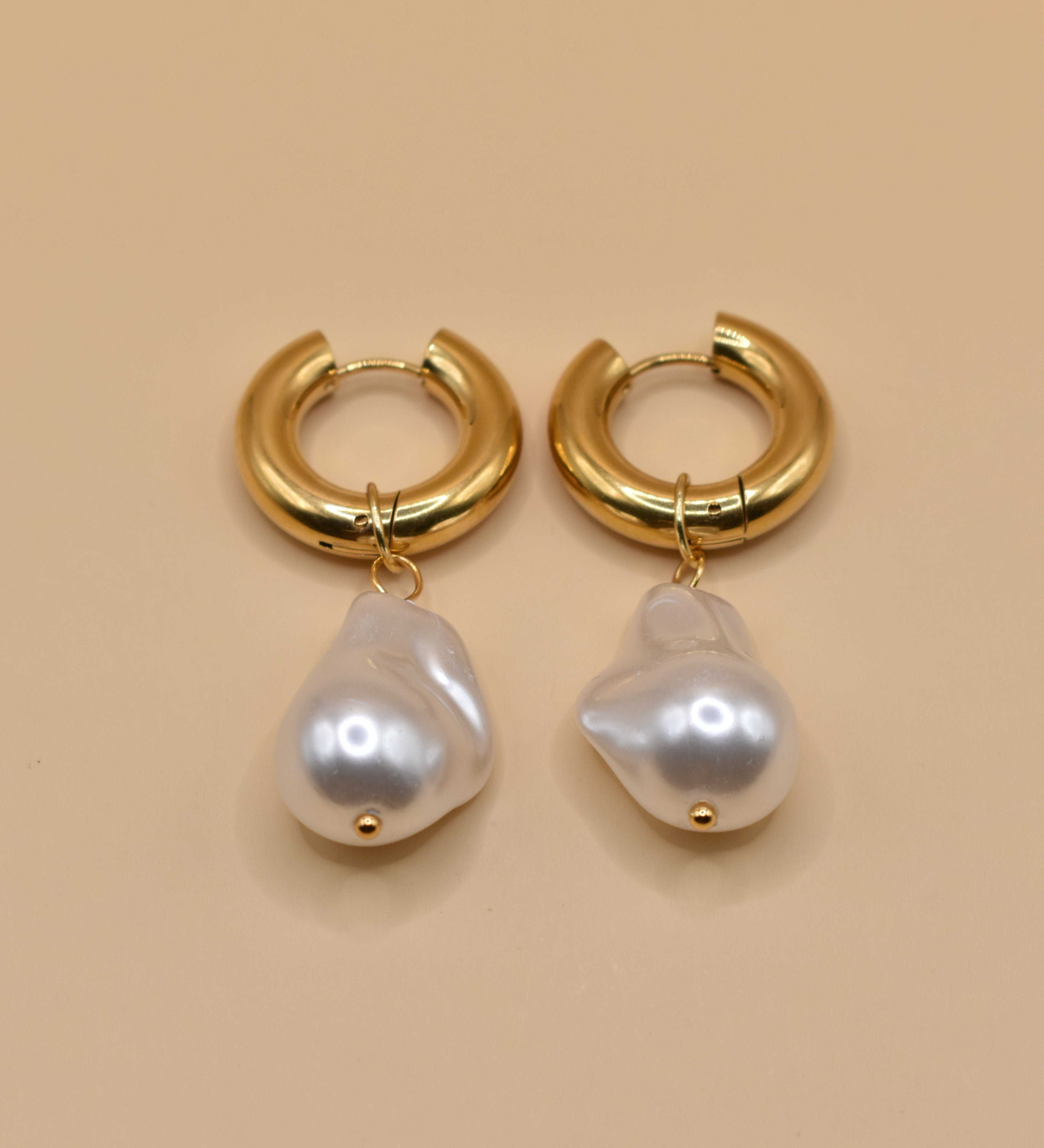 Gold huggies earrings with pearl drop on white background