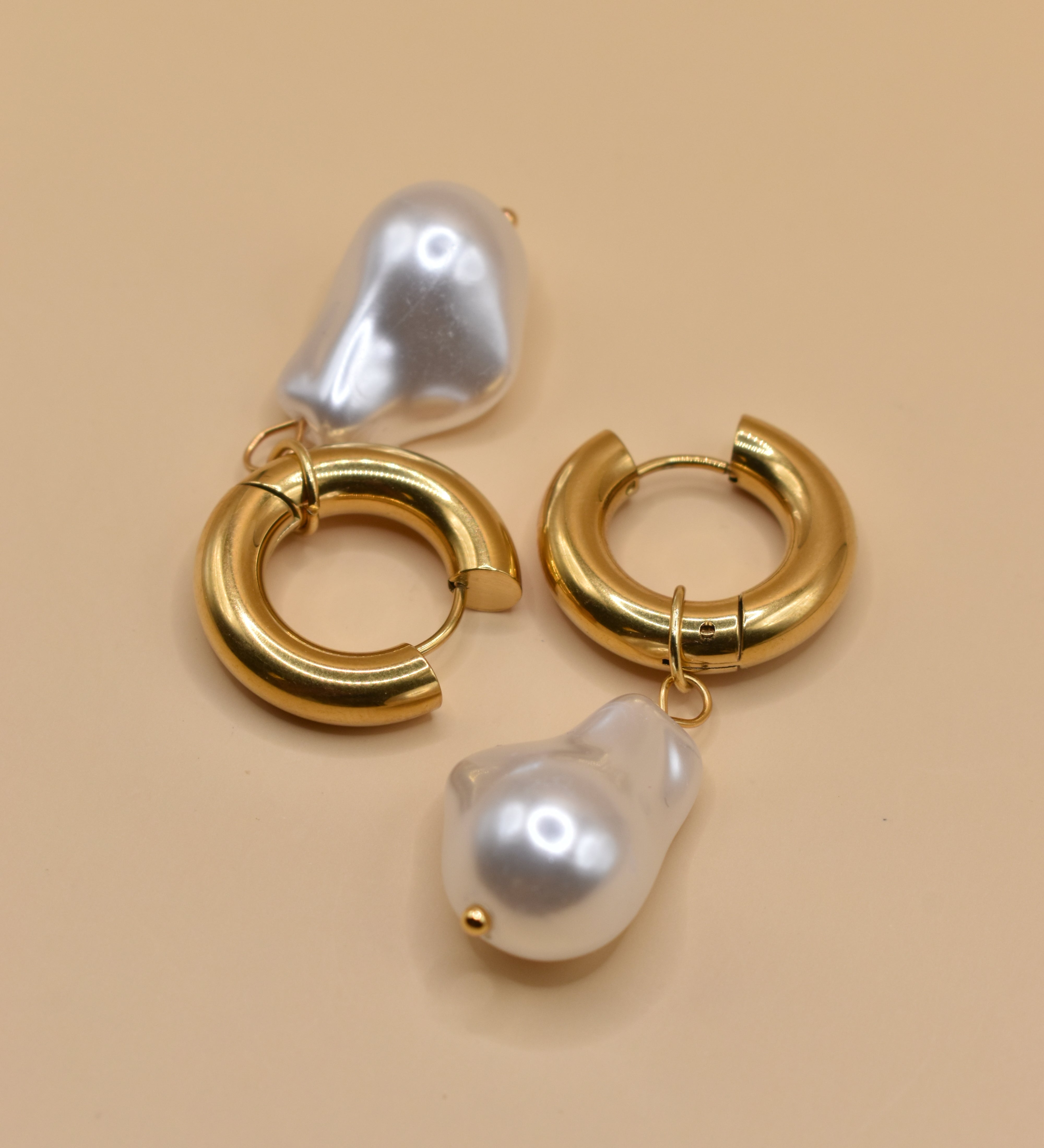 Gold huggies earrings with pearl drop on white background
